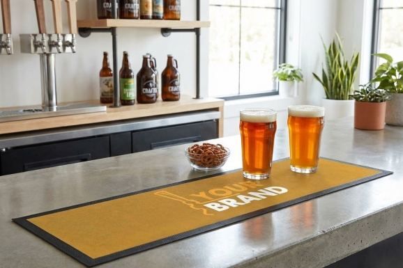 Two pints of craft beer served on a branded bar mat at a taproom counter