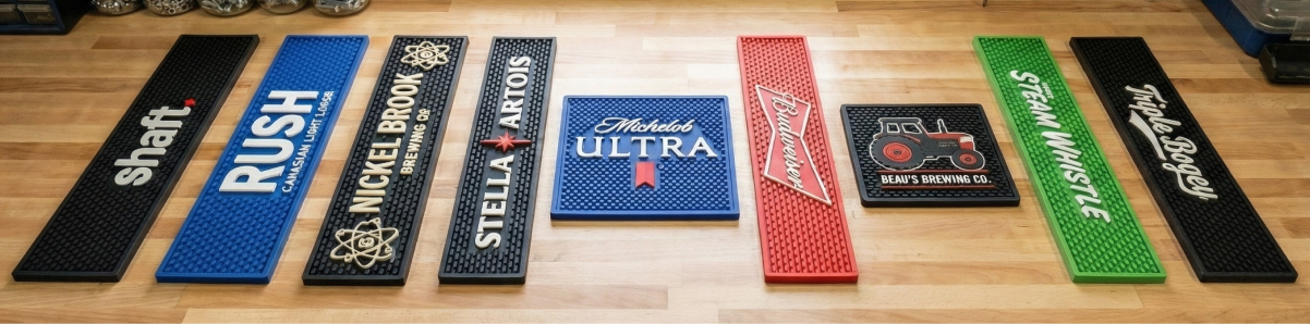 Row of custom bar mats printed with real brewery and brand logos including Rush, Nickel Brook, Stella Artois, Michelob Ultra, Budweiser, Steam Whistle and Triple Bogey
